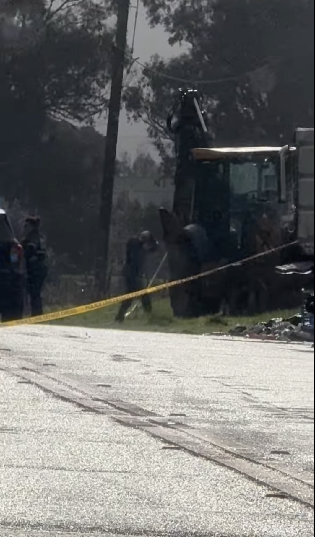 Vallejo police investigators near a cordoned-off area with yellow police tape, operating heavy machinery in a grassy lot. A police vehicle and scattered debris are visible in the background, framed by trees and utility poles.